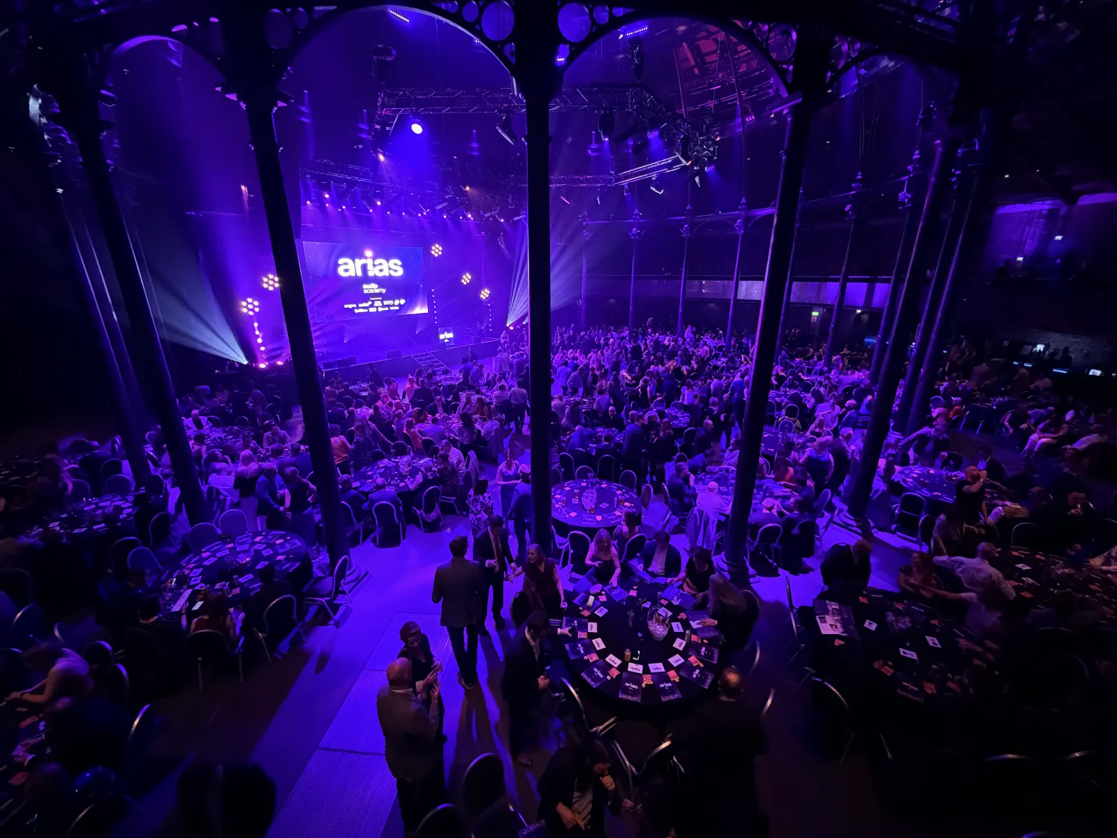 Looking down on the packed Roundhouse from the balcony during the ARIAS, guests at round tables scattered with cards, the stage glowing purple at the far end.